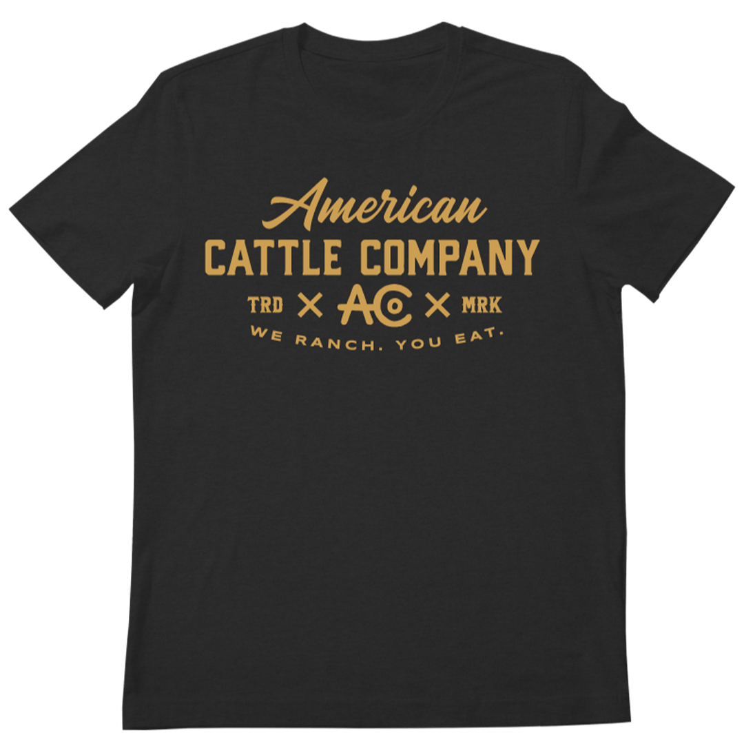 The Rural Cloth We Ranch You Eat Tee-Heather Charcoal features gold “American Cattle Company TRD x AC x MRK” and “We ranch. You eat.” text—ideal for cattle ranching fans supporting American ranchers.