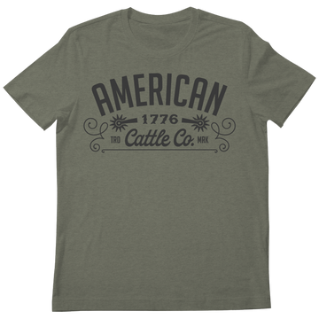 The American Cattle Co Western Tee features “AMERICAN 1776 Cattle Co.” in bold black letters and decorative flourishes on olive green fabric—a classic tribute to the American cattle industry.