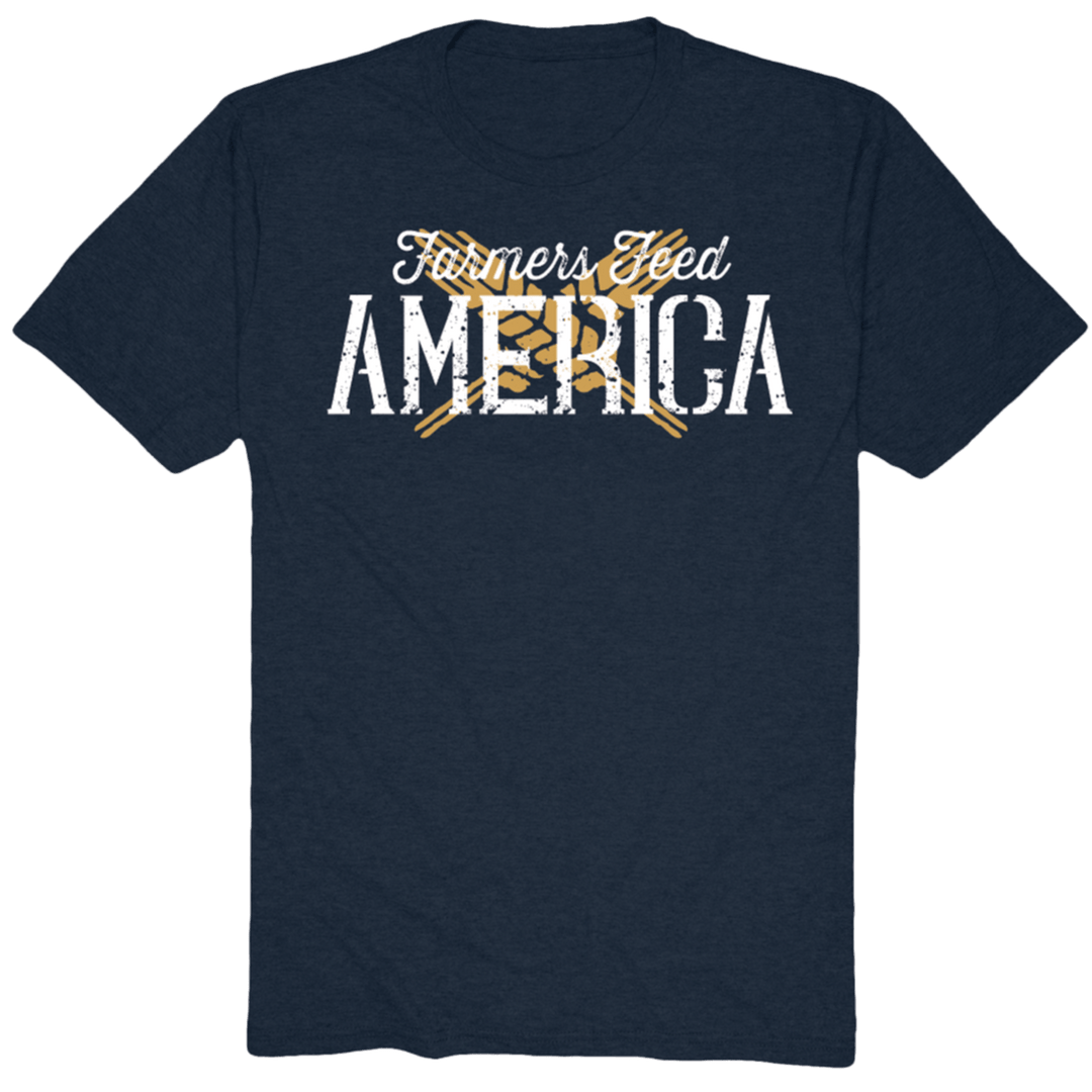 The Wheat X Tee-Heather Navy by American Cattle Co features "Farmers Feed America" in distressed white and yellow text, with crossed yellow pitchforks behind "Feed," celebrating American farmers’ dedication.